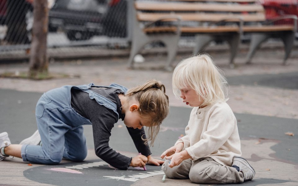 Nieuwsbericht Opgroeien twee kindjes spelen buiten met krijt op de grond
