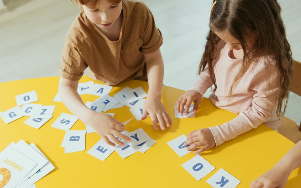 twee kleuters zitten aan een tafel en werken met kaartjes