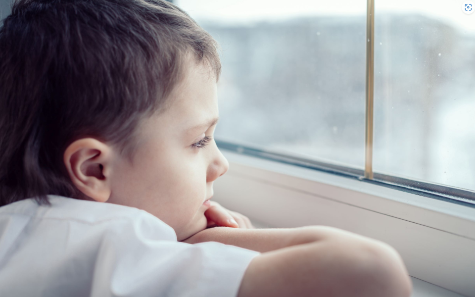 Jongen kijkt uit raam, is droevig