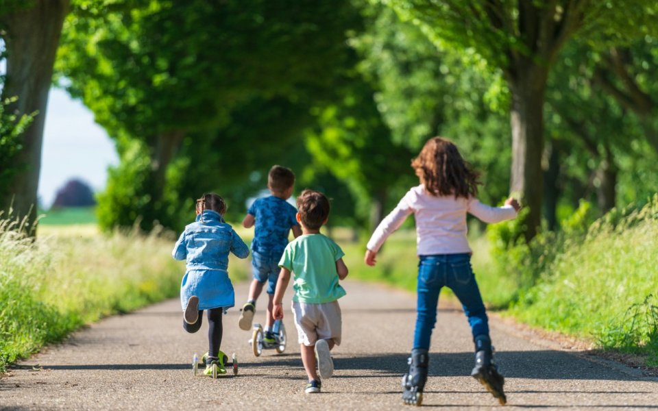 Kinderen met step, skateboard, rolschaatsen en al lopend op een pad
