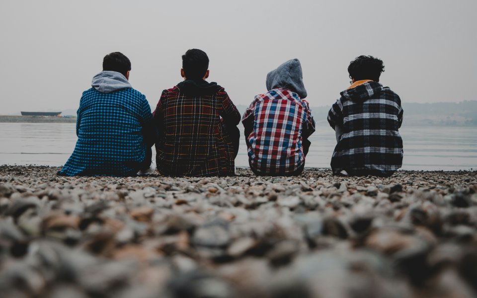 Vier jongeren zitten aan zee op het strand met hun rug naar de camera