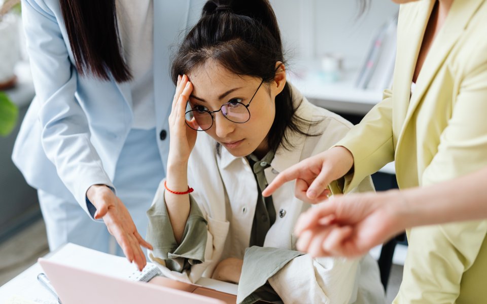 vrouw-in-werkcontext-die-gefrustreerd-kijkt--collega-s-wijzen-naar-haar