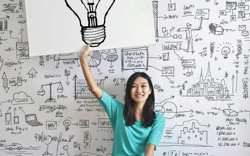 vrouw-voor-muur-vol-ideen-en-formules-met-papier-in-de-hand-met-gloeilamp-op-getekend