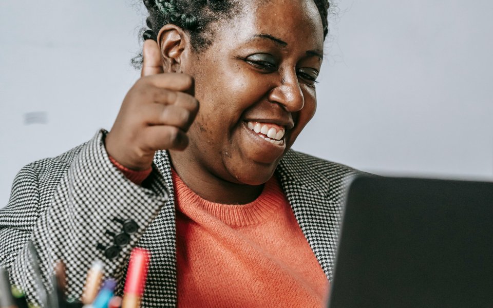 vrouw zicht achter haar pc en steekt duim omhoog 