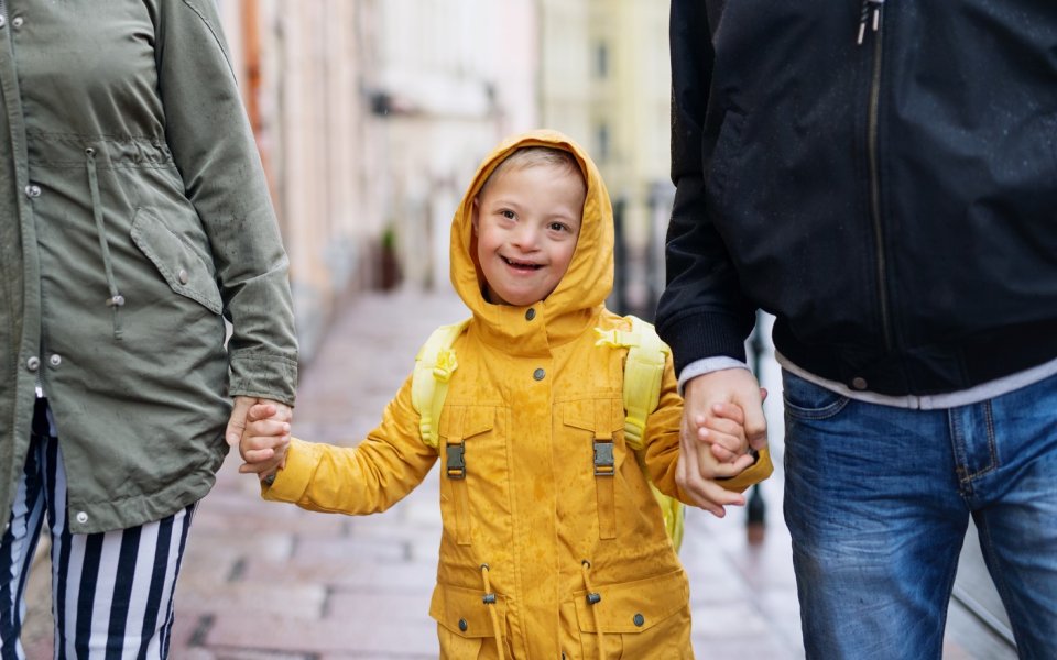 Jongen met downsyndroom wandelt met 2 volwassenen terwijl het regent
