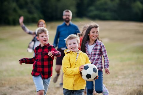 Kinderen spelen buiten met een voetbal, begeleiders op de achtergrond