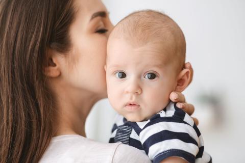 Moeder in close-up die haar baby een kus op de wang geeft. De baby kijkt naar de camera.