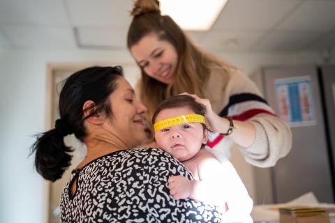 Verpleegkundige meet hoofdomtrek baby in armen van ouder op consultatiebureau Kind en Gezin