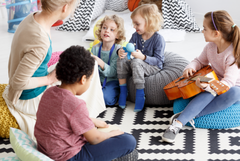 Groep kinderen en begeleider zitten samen in de kring en maken muziek