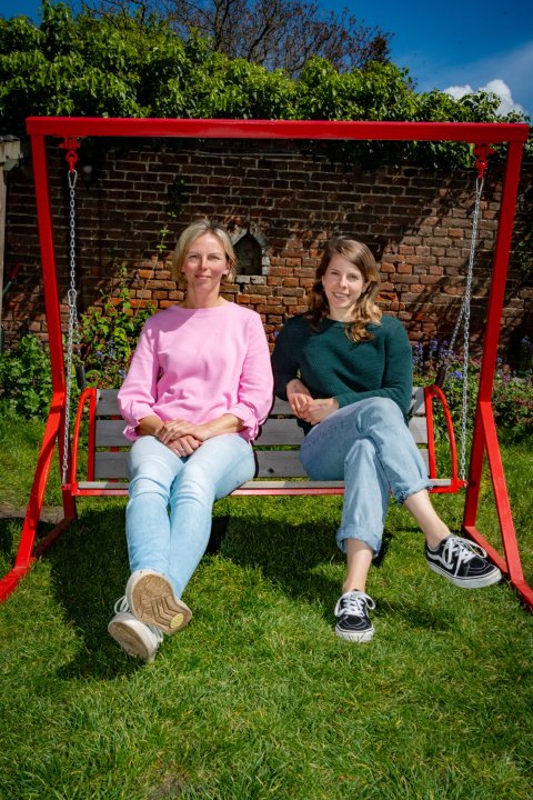 Heleen en Tine zitten samen buiten op een schommel