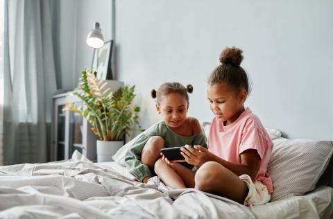 Twee jonge meisjes bekijken samen iets op smartphone in de zetel