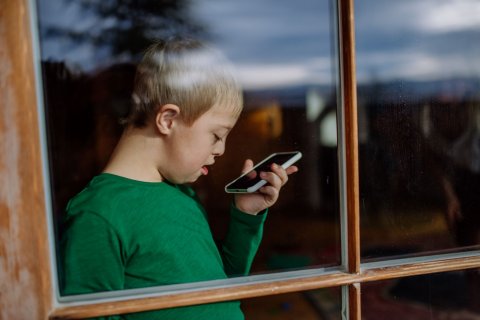 Jongen met downsyndroom, beperking, zorgbehoefte gebruikt zijn smartphone