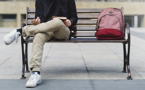 Jongen zit op een bank met een rode rugzak naast hem