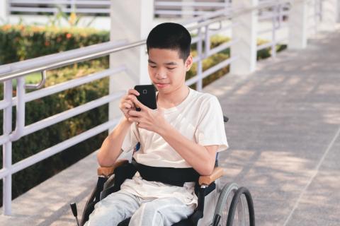 Tienerjongen met ondersteuningsnood in rolstoel scrollt op zijn smartphone
