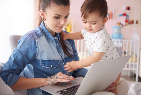mama in jeanshemd werkt op laptop met kind op de schoot