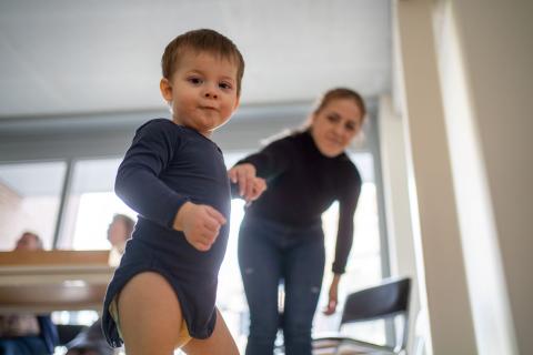 Een peuter stapt rond in een consultatiebureau, zijn mama geeft hem een hand