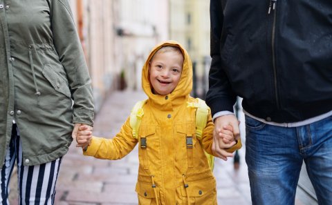 Jongen met downsyndroom wandelt met 2 volwassenen terwijl het regent